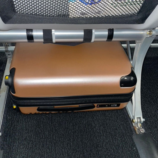 An image of the rose gold Take OFF Luggage Personal Item 2.0 Underneath the seat in front of the passenger's seat.
