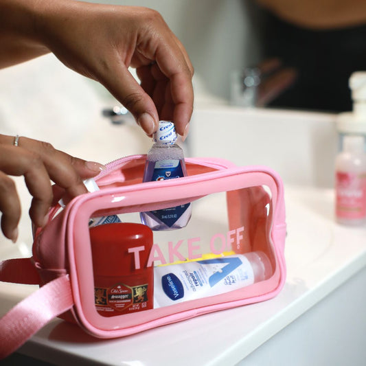 Person places a travel-sized mouth wash bottle into the Take OFF Big Toiletry pouch algonside a travel sized deodorant and travel size bottle of lotion