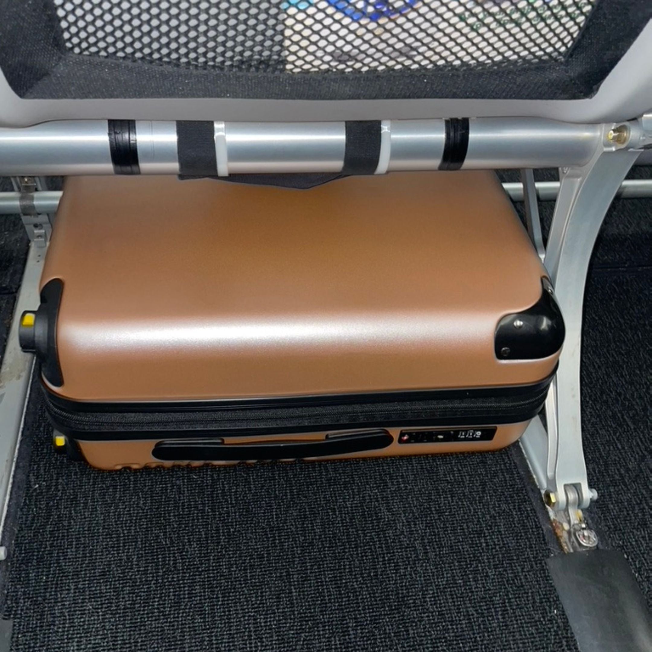 An image of the rose gold Take OFF Luggage Personal Item 2.0 Underneath the seat in front of the passenger's seat. 